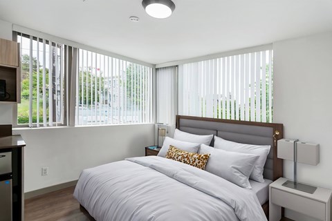 A bedroom with a large bed and a window with blinds.