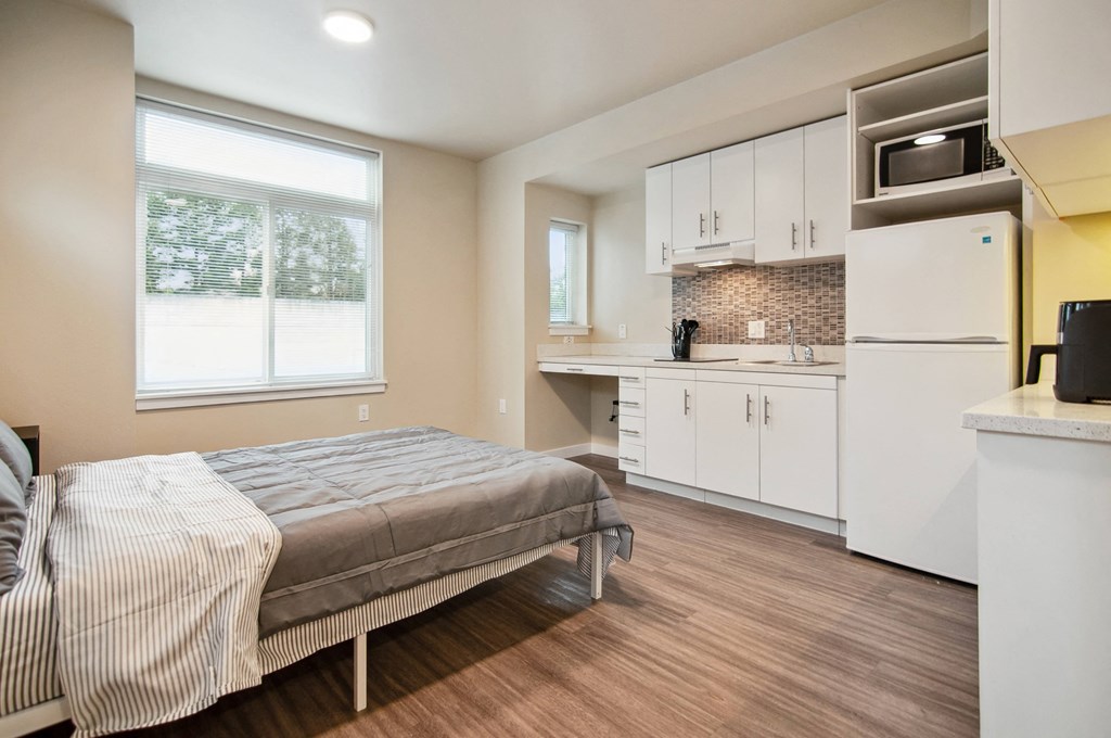 A bedroom with a bed, a kitchen, and a window.