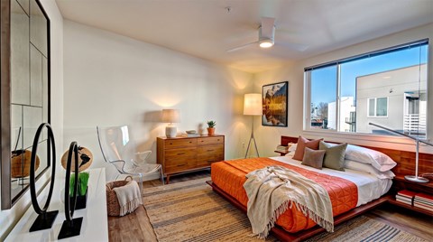 Bedroom with a platform bed, wood dresser, ceiling fan, and a large window looking out to the neighborhood.