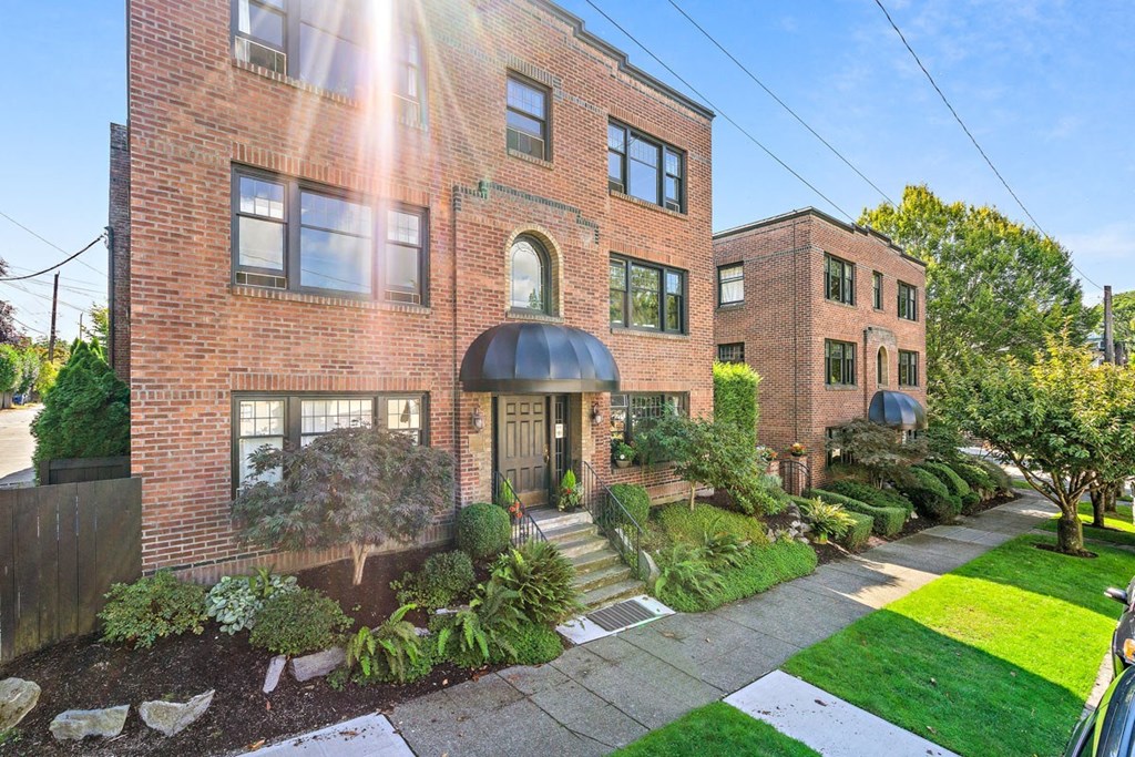 the front of a brick apartment building with a sidewalk and grass