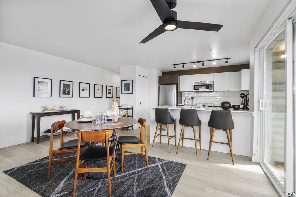 a dining area with a wooden table and chairs and a kitchen in the background