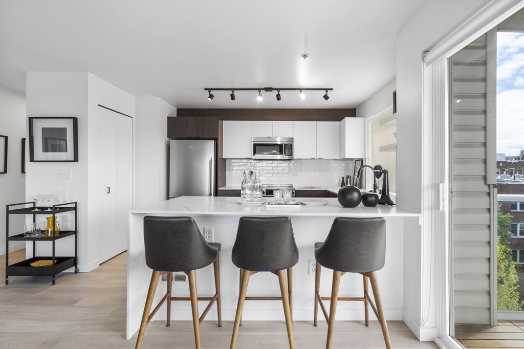 a kitchen with white cabinetry and a large island with three stools in front of it