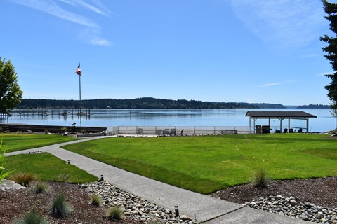 a grassy area with a flagpole and benches next to a body of water