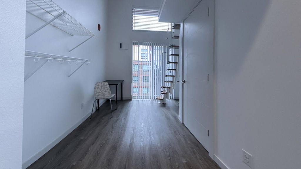 an empty room with a staircase and a window and white walls and wood floors