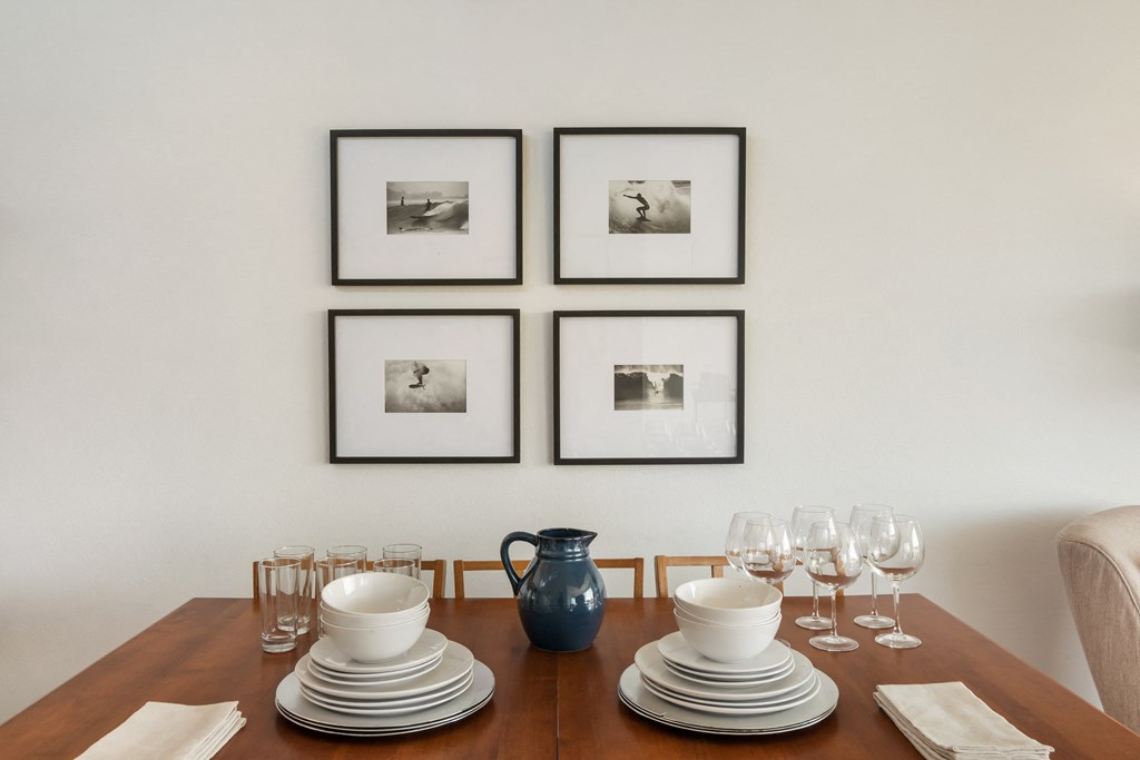 a dining table with plates and glasses on it and four pictures on the wall above