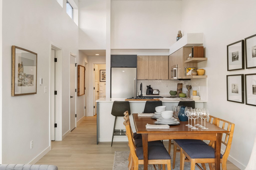 a dining area with a wooden table and chairs and a kitchen in the background