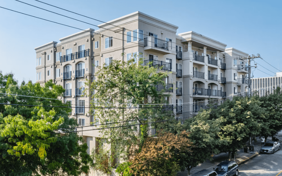 A large white building with balconies and trees in front.