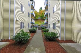 a sidewalk leading to an apartment building with a grassy hill in the background