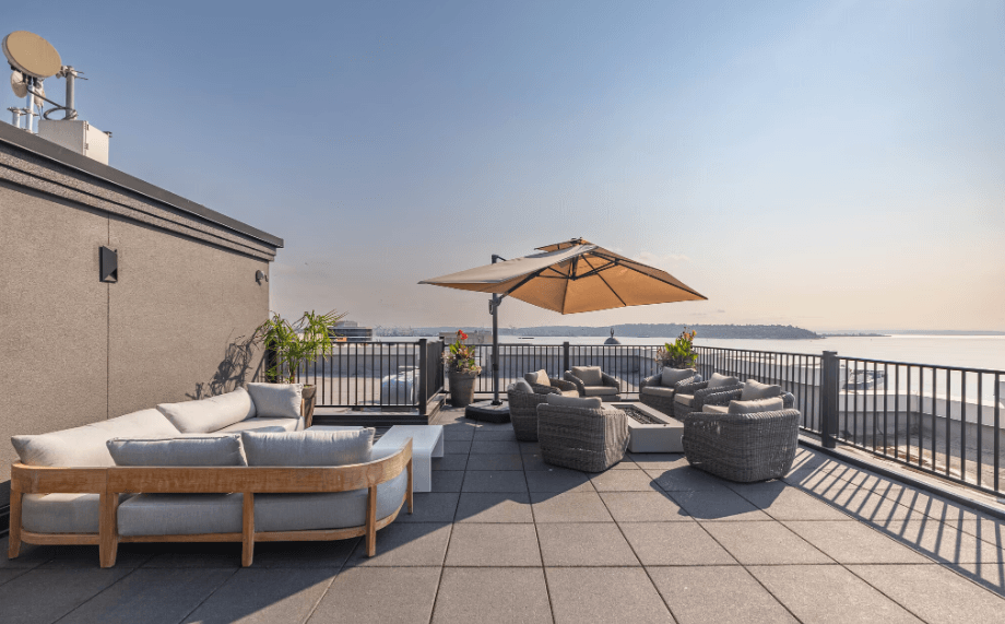 A patio with a couch, chairs, and an umbrella overlooking a body of water.