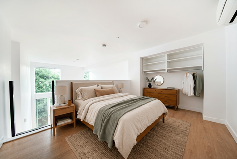 A bedroom with a large bed and a dresser with clothes hanging on it.
