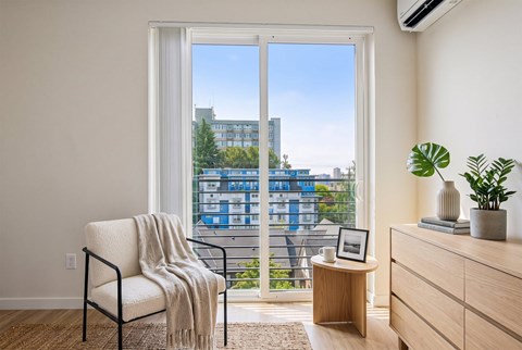 A chair with a blanket draped over it sits in front of a large window with a view of a cityscape.
