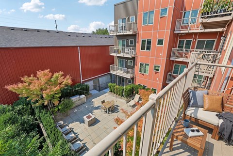 A balcony with a table and chairs overlooks a courtyard with a tree.