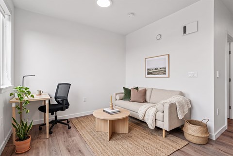 Living room with a sofa, jute rug, and a desk and task chair set up as a home office nook.