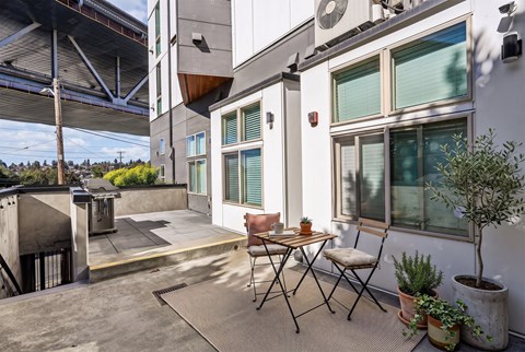 Paved courtyard patio with a bistro table and chairs, potted plants and a gas grill on the upper terrace.