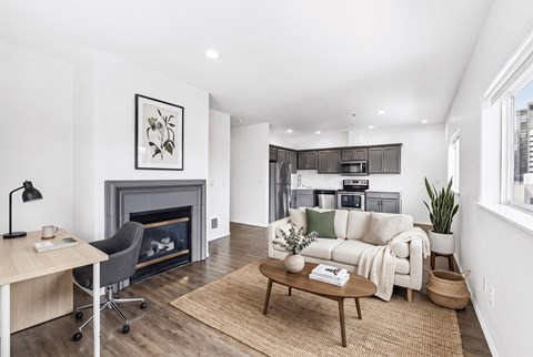 Open living room with a tiled fireplace, a work desk, and a kitchen with stainless appliances beyond.