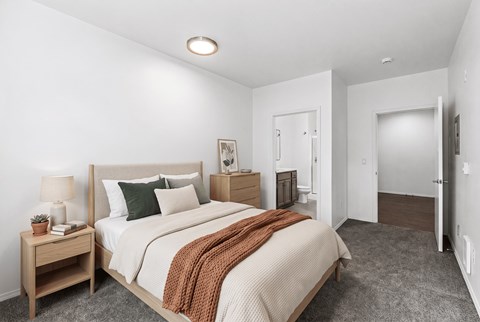 Carpeted bedroom with a queen bed and a dresser, with a doorway into an ensuite bathroom.
