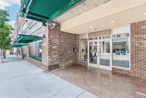 Entrance to Hawthorne Apartments with glass doors, brick walls, green awnings, and the number 1618.