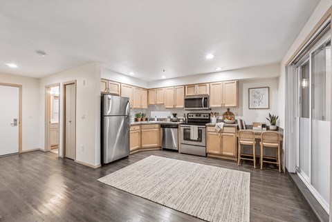Kitchen with maple cabinets, stainless appliances, and a breakfast bar with two stools, beside the entry.