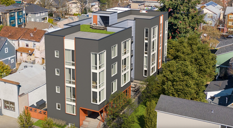 A modern building with a green roof is surrounded by other buildings.