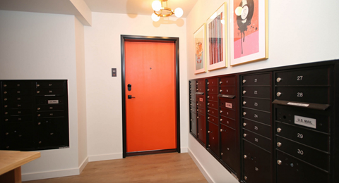 A hallway with a red door and mailboxes on the wall.