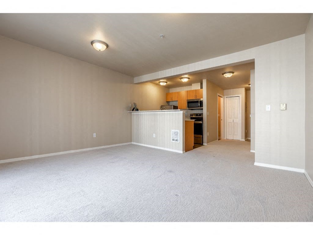 an empty living room with a kitchen in the background
