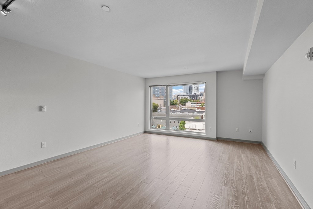 Empty room with wooden flooring and a window overlooking a cityscape.