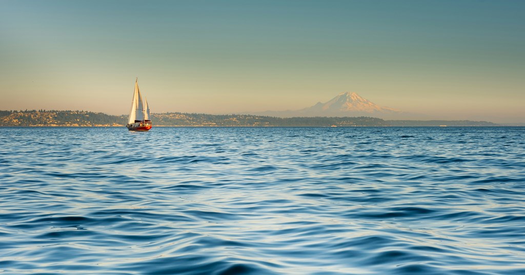 A sailboat is sailing on the water with a mountain in the background.