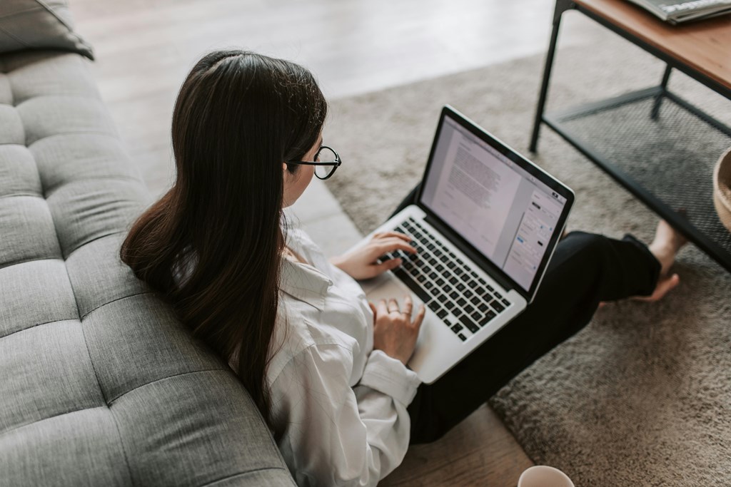 A woman is sitting on a couch using a laptop.