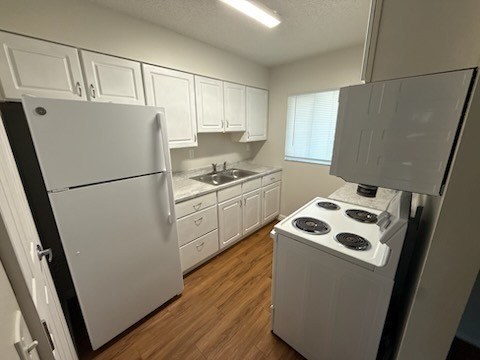 A white refrigerator stands in a kitchen with wooden floors and white cabinets.
