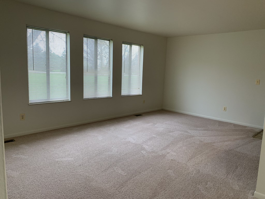 the living room of an empty house with three windows