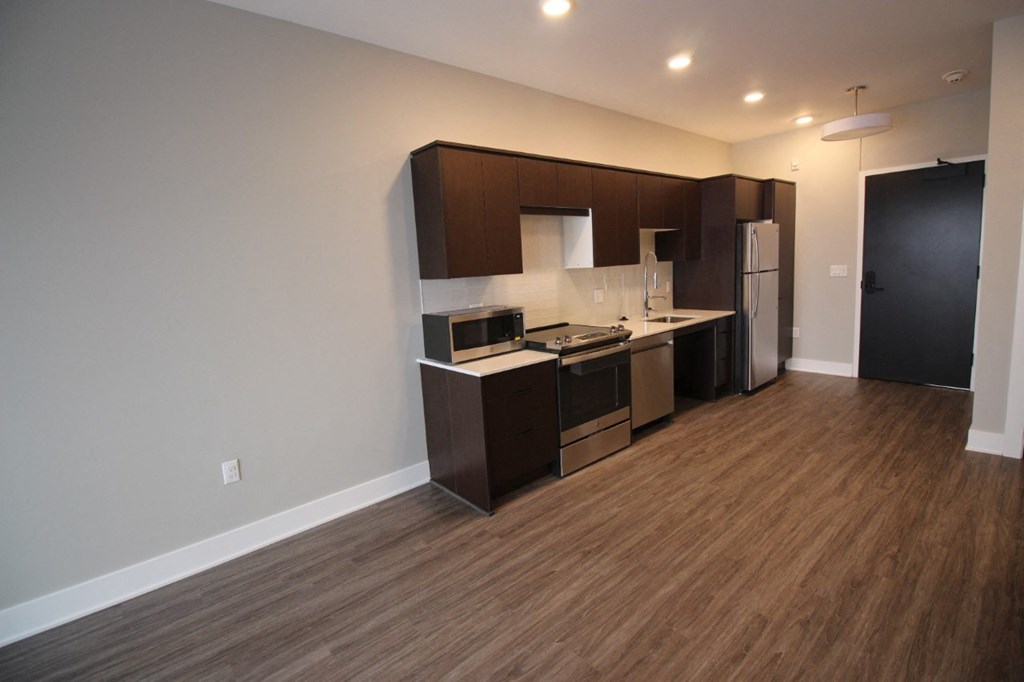 an empty living room with a kitchen with wood flooring and