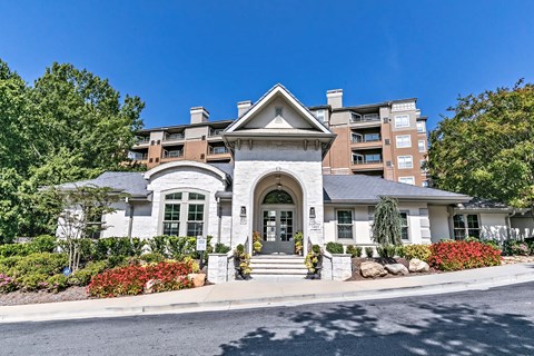 west-paces-entrance-building-landscaping-atlanta-ga.jpg: Stone-arched clubhouse entrance with red flower beds and a mid-rise apartment building at 1401 West Paces