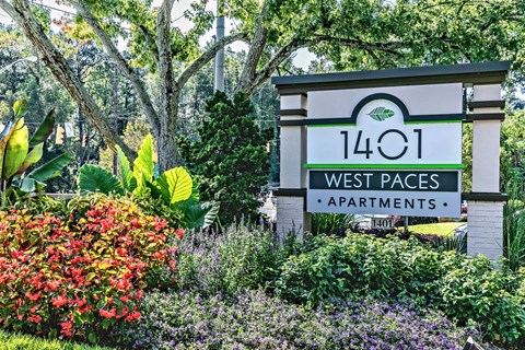 A sign for 1401 West Paces Apartments is surrounded by flowers and greenery.