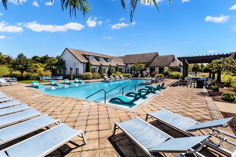 A pool surrounded by lounge chairs and a house in the background.