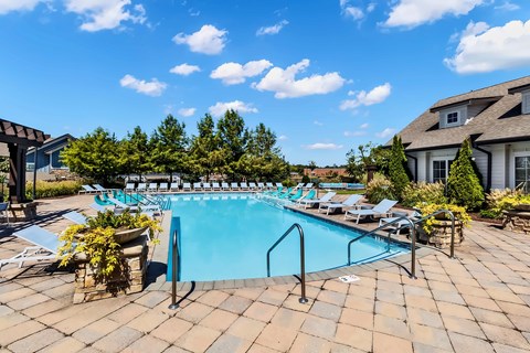 A large outdoor swimming pool surrounded by lounge chairs and potted plants.