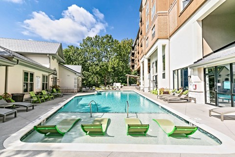 A swimming pool with green lounge chairs and a building in the background.
