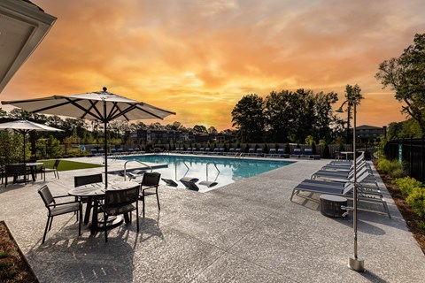 a swimming pool with chairs and umbrellas at sunset