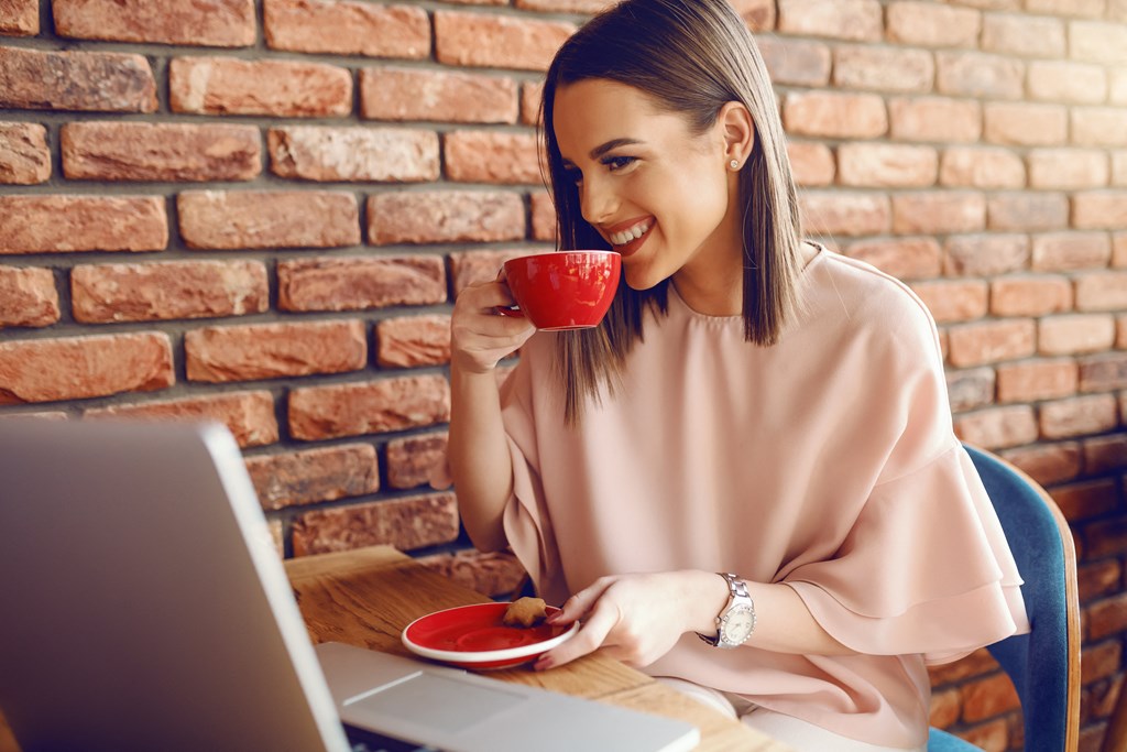 a woman sitting at a table with a laptop and a cup of coffee