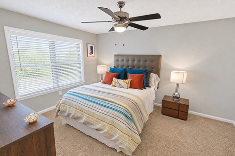 A bedroom with a bed, a ceiling fan, and two lamps.