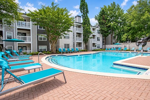 A swimming pool surrounded by blue lounge chairs and trees.