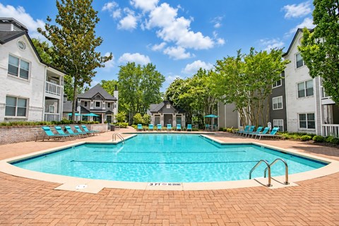 A swimming pool surrounded by chairs and trees in a residential area.