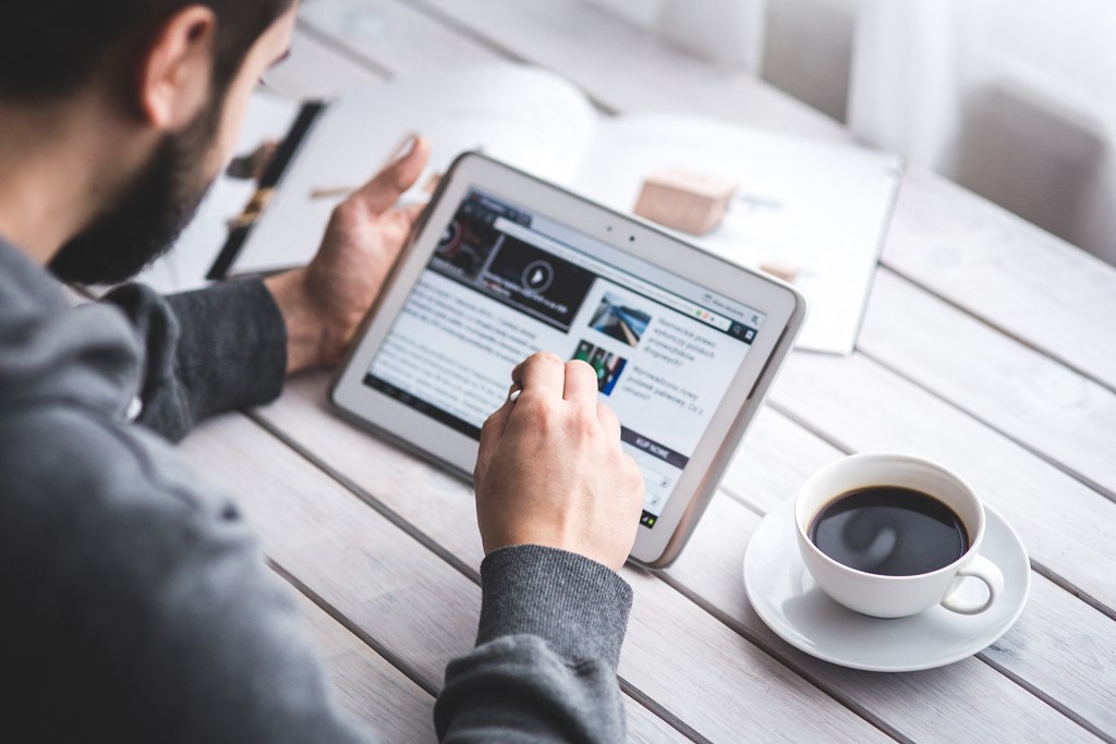 a man sitting at a table with a cup of coffee using a tablet computer