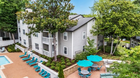A pool surrounded by chairs and umbrellas is in front of a building.