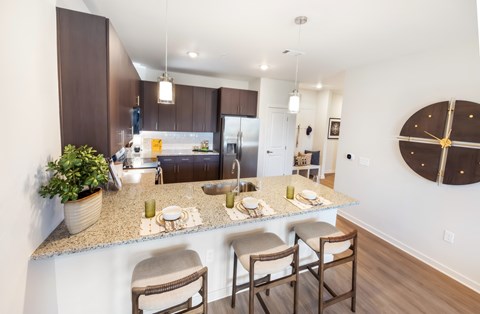 A kitchen with a counter and chairs in the foreground and a dining area in the background.