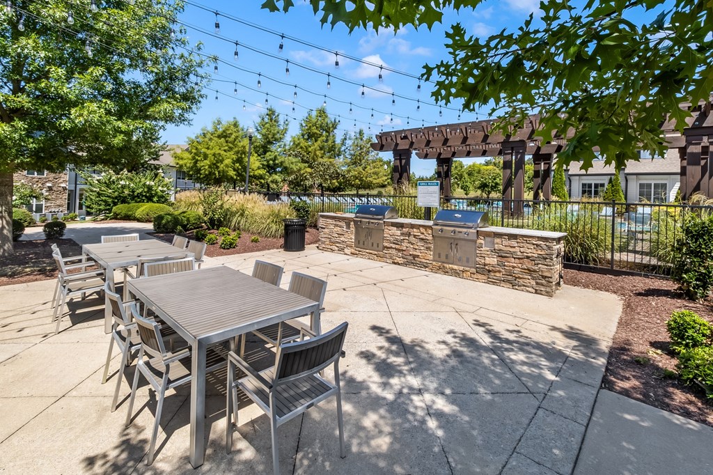 A patio with a table and chairs is surrounded by greenery and a stone wall.
