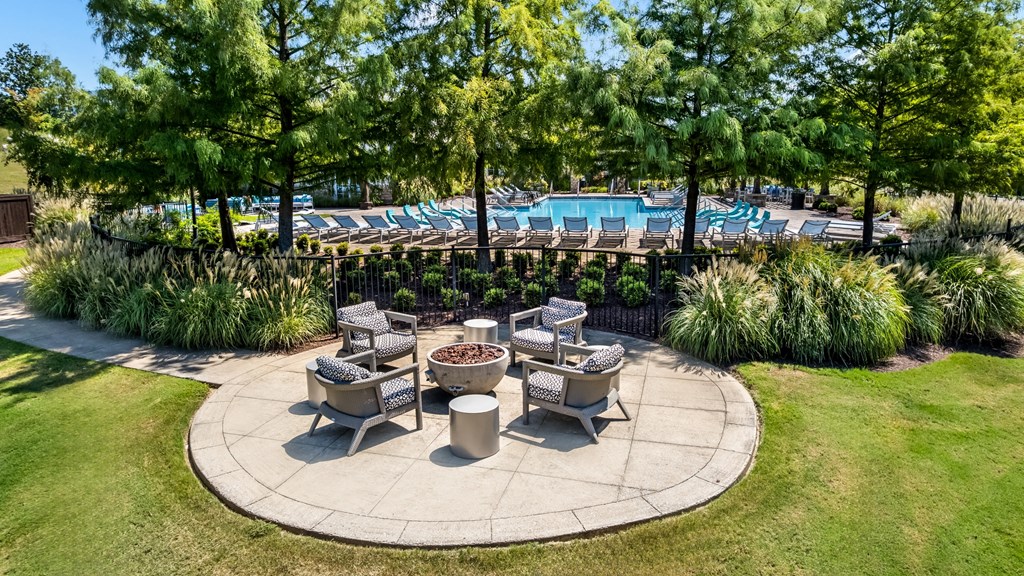 A round patio area with a fire pit surrounded by chairs and trees.