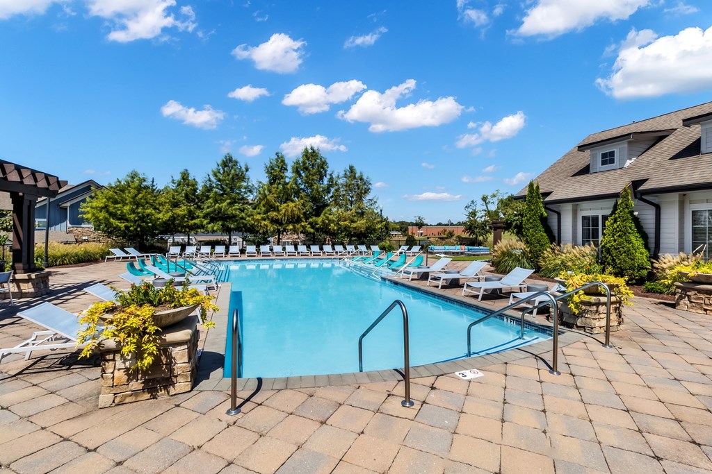 A large outdoor swimming pool surrounded by lounge chairs and potted plants.