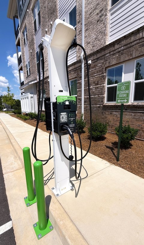 A green and white electric vehicle charging station on a sidewalk.