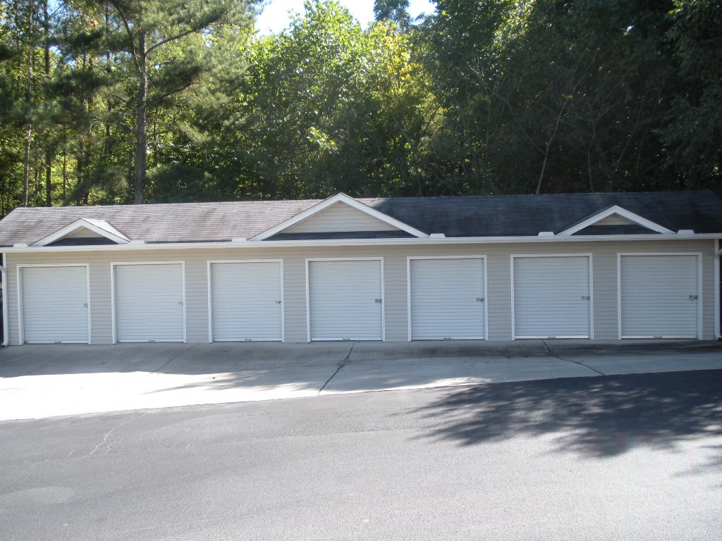 A building with white garage doors in front of a wooded area.