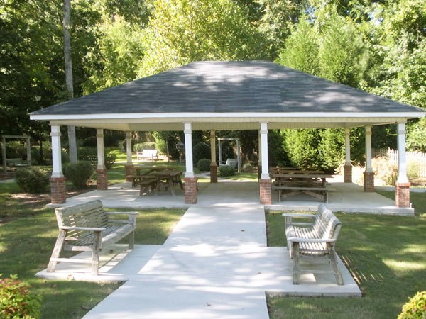 A gazebo with a white roof and four pillars is surrounded by a white walkway and four benches.